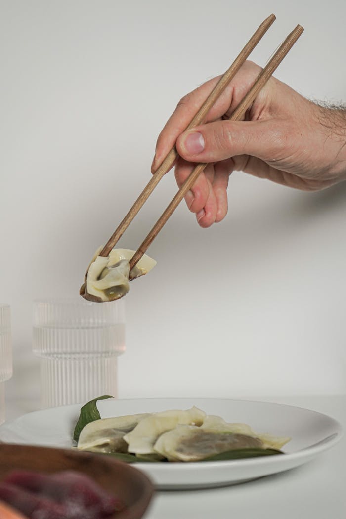 A hand holding chopsticks with a dumpling. Minimalist close-up food photography.